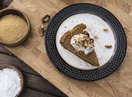 A slice of pumpkin pie with whipped cream and nuts on a plate.
