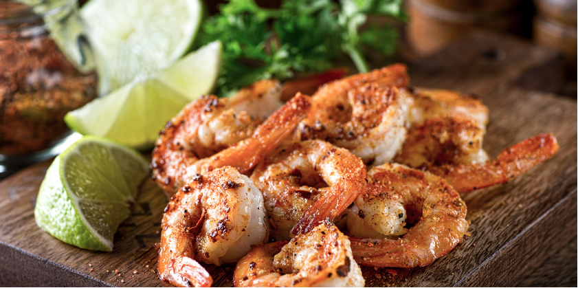 A wooden cutting board topped with shrimp and lime wedges.