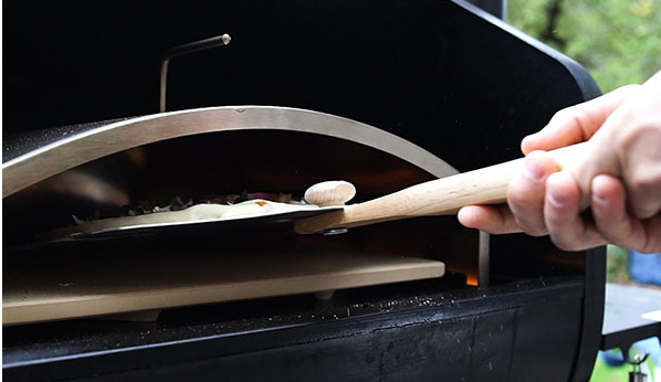 A person is putting a pizza into a pizza oven with a spatula.