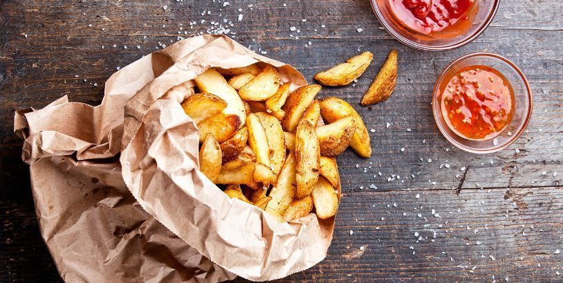 A bag of french fries is sitting on a wooden table next to a bowl of ketchup.