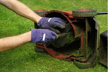 A person is cleaning the inside of a lawn mower.