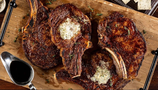 A wooden cutting board topped with two steaks and a spoon of gravy.