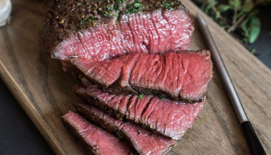 A piece of roast beef is sitting on a wooden cutting board.