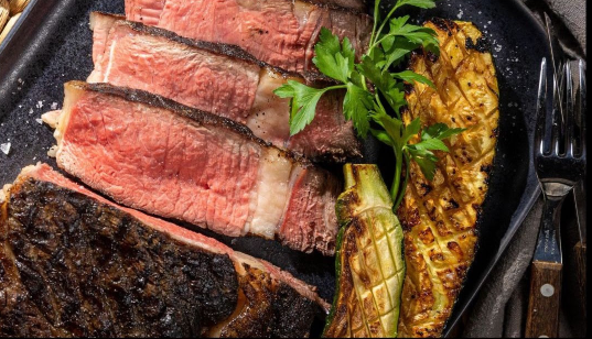 A close up of a plate of food with meat and vegetables on a table.