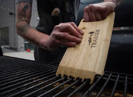 A man is cleaning a grill with a wooden spatula.