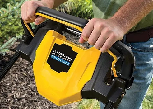 A man is holding the handle of a yellow and black lawn mower.