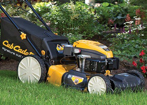 A yellow and black cub cadet lawn mower is sitting on top of a lush green lawn.