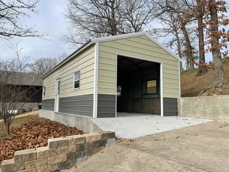 Small beige-and-gray detached garage or shed with open front entrance and concrete driveway.