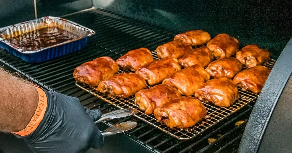 A person is cooking chicken on a grill.