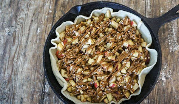A skillet filled with apples and caramel sauce on a wooden table.