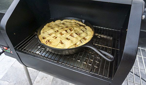 A pie is cooking on a grill in a skillet.