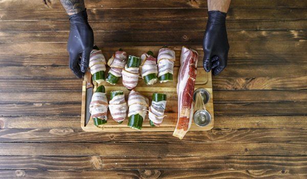 A person is wrapping chicken in bacon on a wooden cutting board.