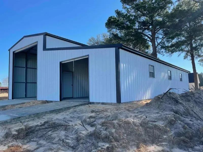 White metal warehouse building with large open bays on a dirt lot under a clear blue sky