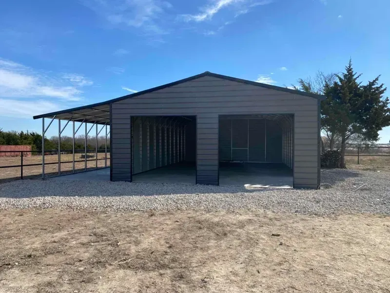 Gray metal carport and garage with open bays on a gravel lot under a blue sky.