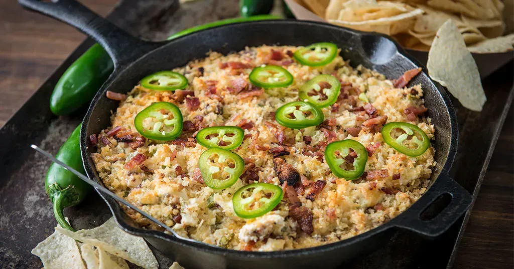 a skillet filled with a dip with jalapenos and chips on a table .