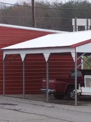 Red metal carport beside a red building, with a red pickup truck parked underneath.