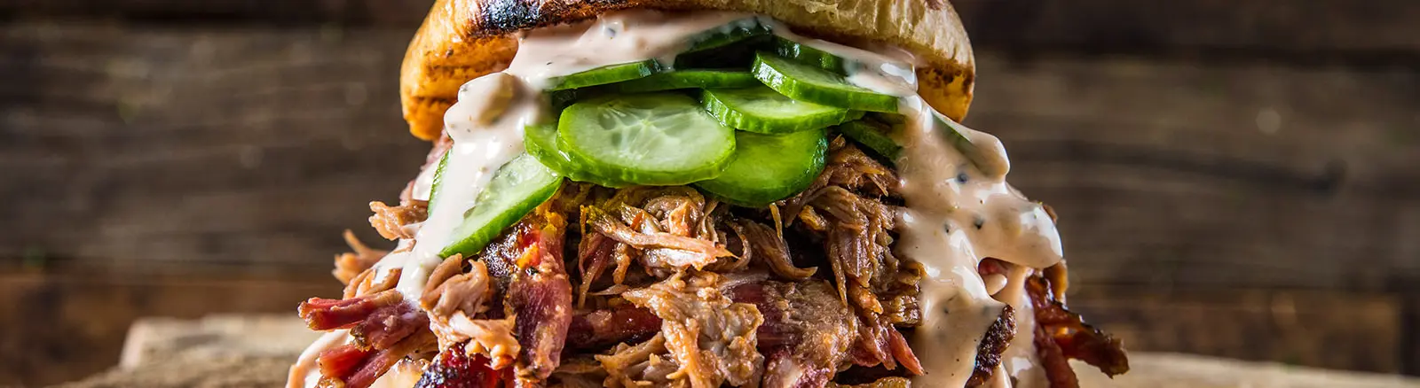 A close up of a pulled pork sandwich on a wooden table.