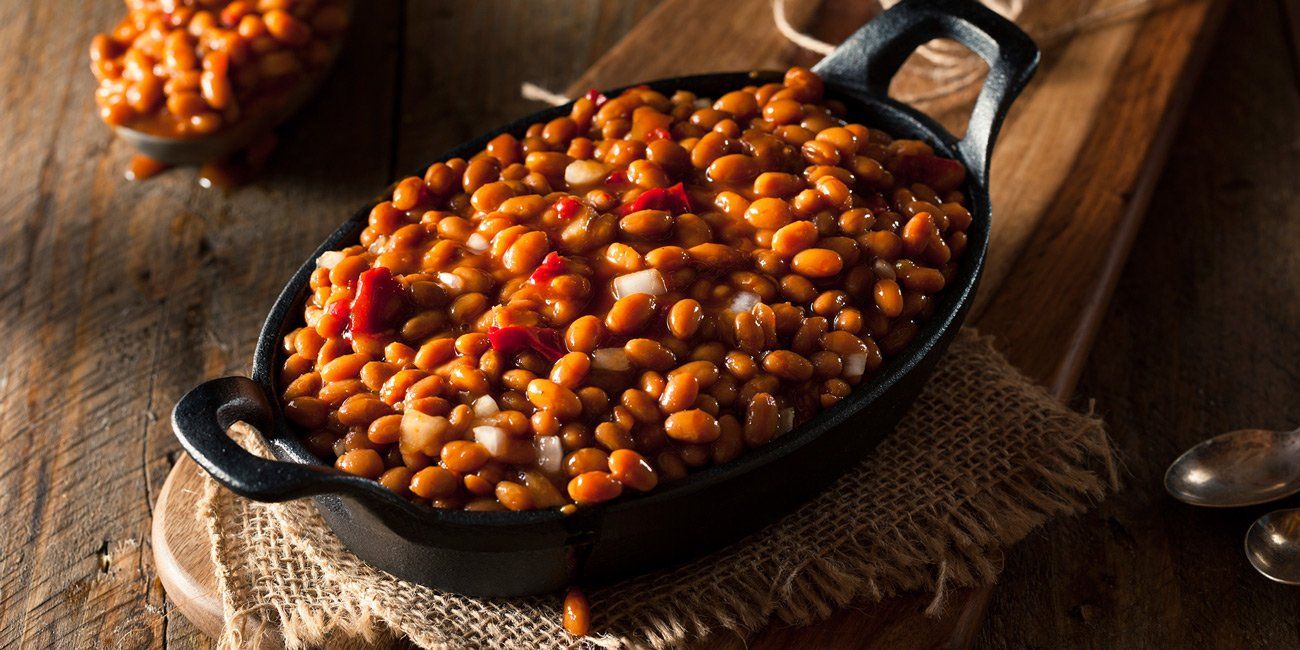 A bowl of baked beans is sitting on a wooden table.
