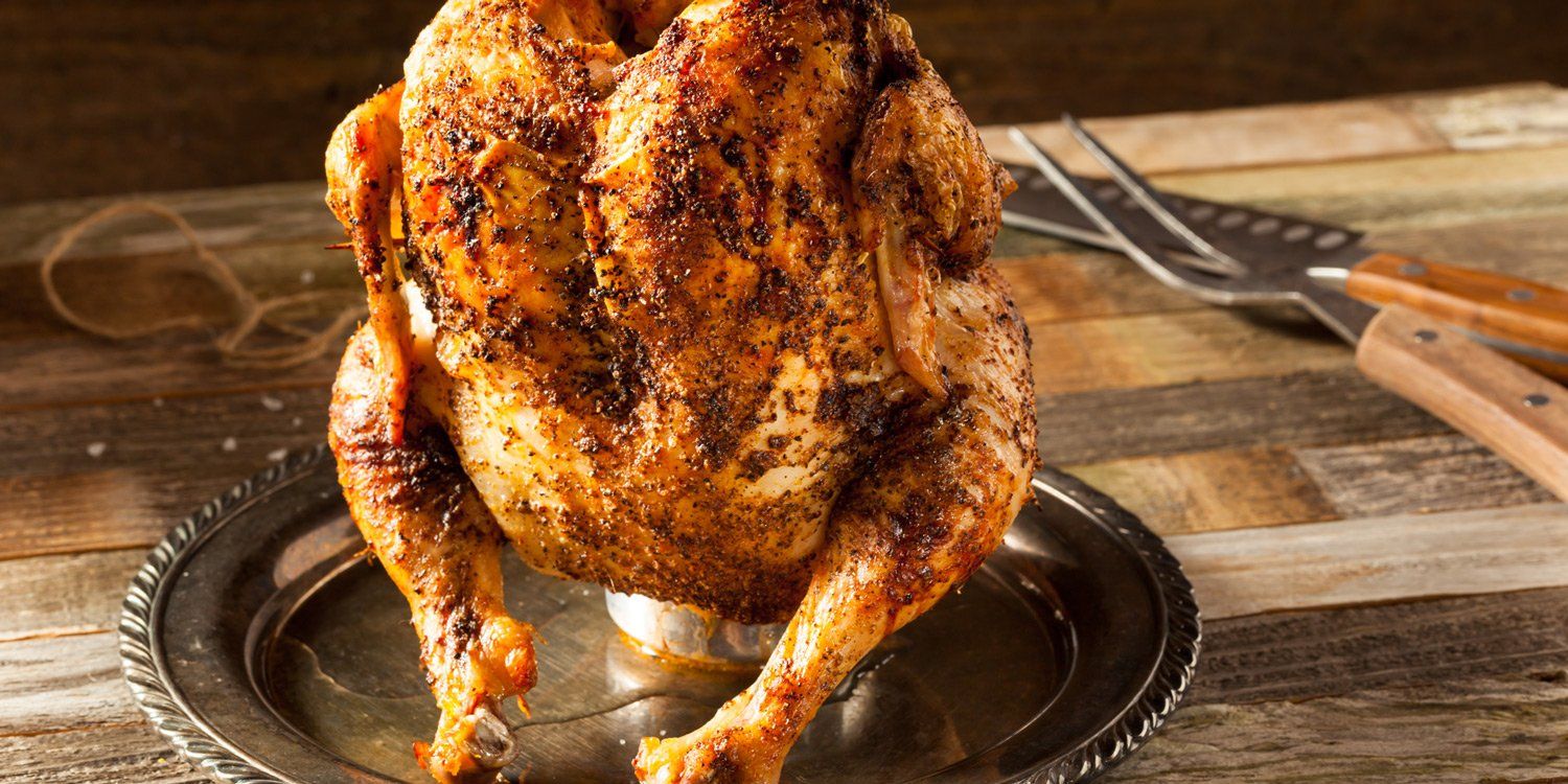 A roasted chicken is sitting on top of a silver plate on a wooden table.