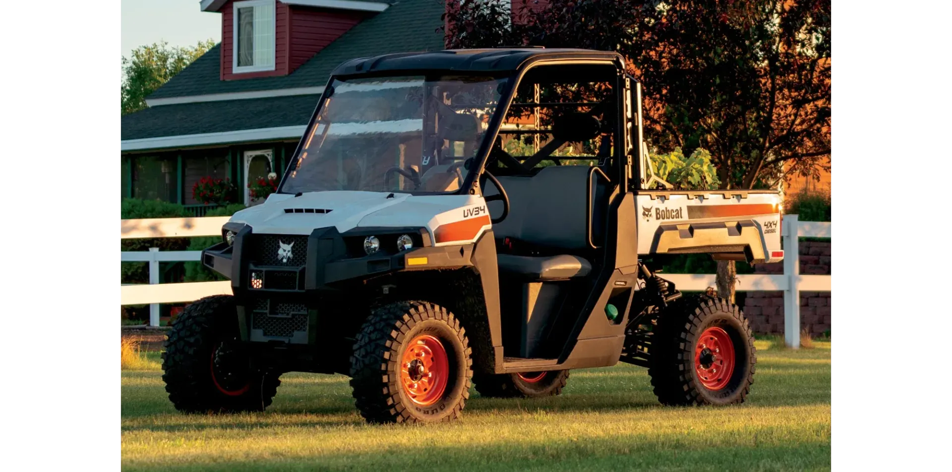 A bobcat utility vehicle is parked in a grassy field in front of a house.