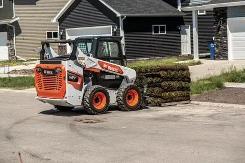 a bobcat skid steer is carrying a pile of grass on the side of the road .