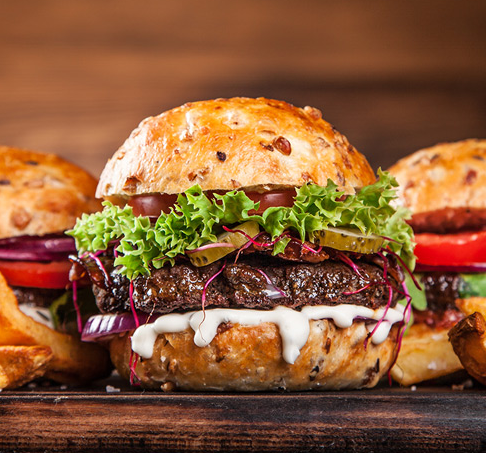 A close up of a hamburger with lettuce , tomatoes , onions and french fries on a wooden table.