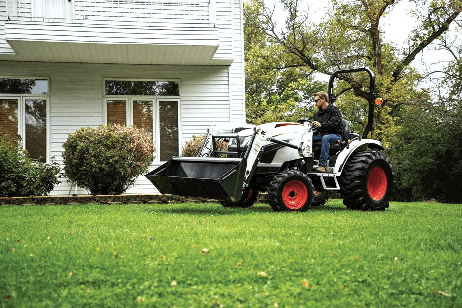 a man is driving a Bobcat CT2025 tractor in a field with cows in the background .