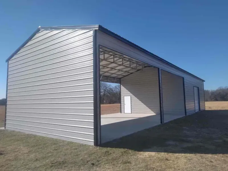 Large metal-sided open-sided shed with a peaked roof on a grassy field under a blue sky