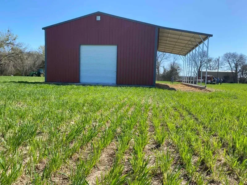 Red barn with a white roll-up door in a grassy field under a clear blue sky