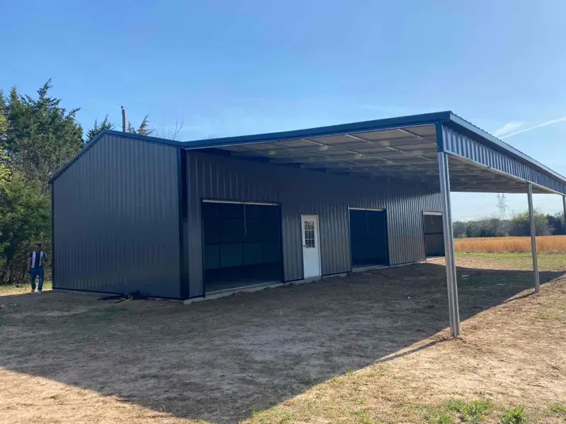 Large metal shed with a covered open front on a dirt lot, blue sky overhead