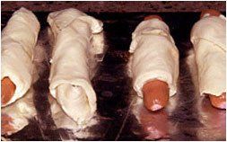 a bunch of hot dogs wrapped in dough on a pan .