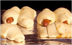 a bunch of hot dogs wrapped in dough on a table .
