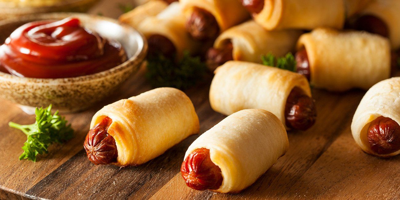 a bunch of hot dogs wrapped in dough on a wooden table .