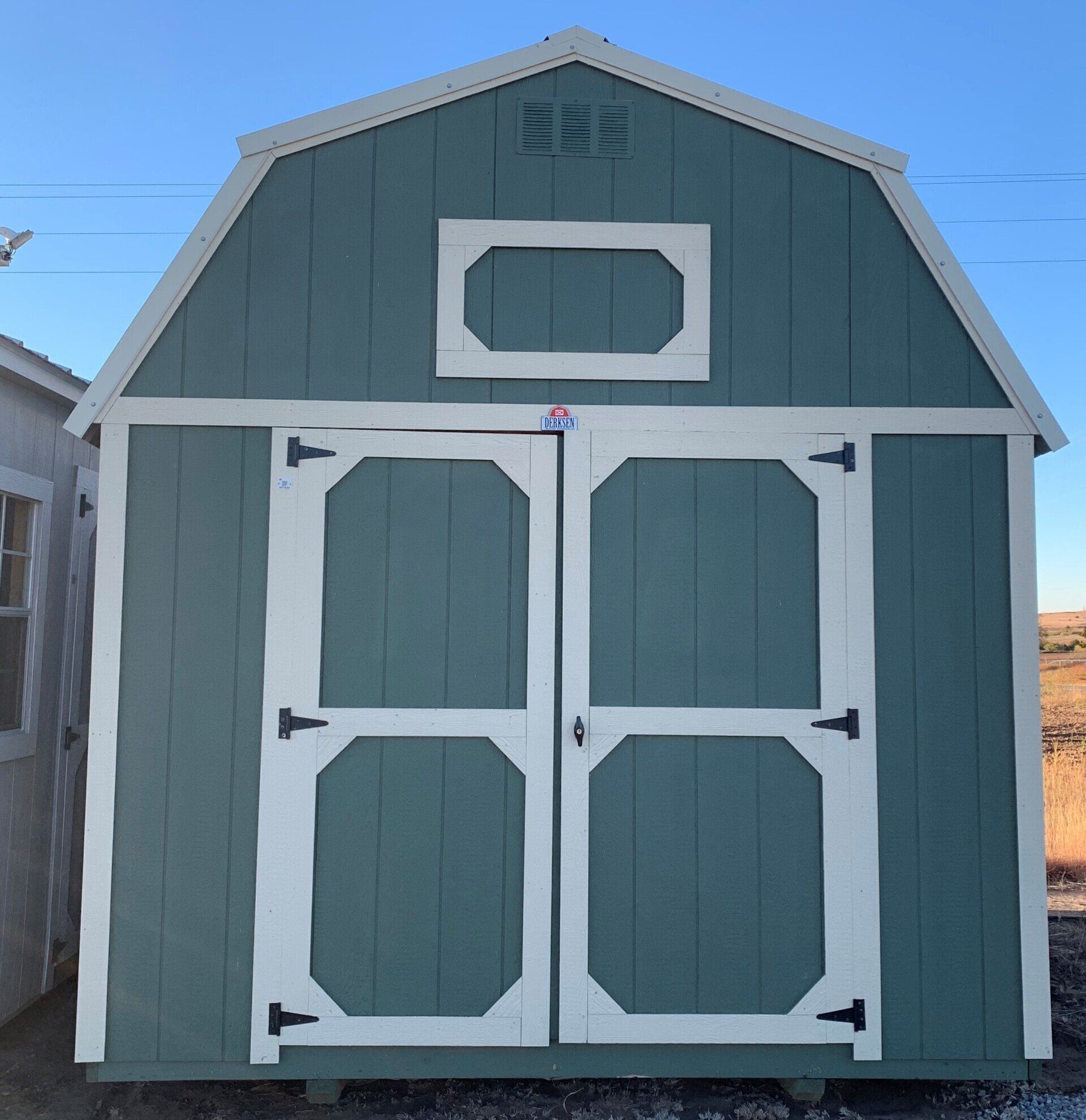 Un cobertizo de granero verde con puertas y ventanas blancas