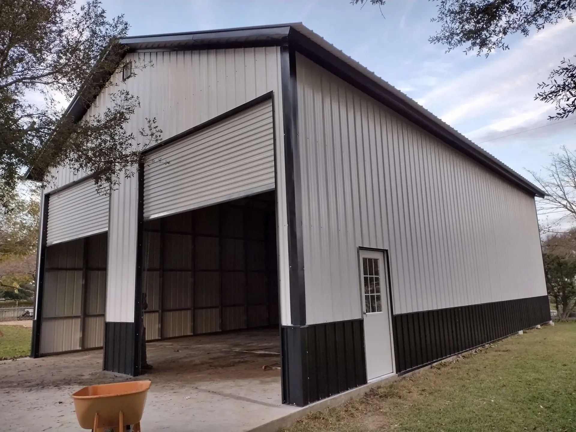 White metal barn with open bay doors and a small side door on a grassy lot