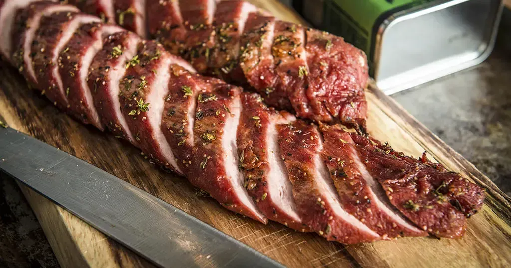 A smoked pork on a wooden board next to a knife 