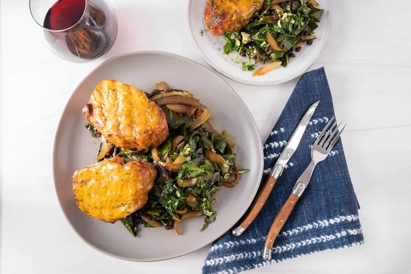 A plate of food with chicken and spinach on a table next to a glass of wine.