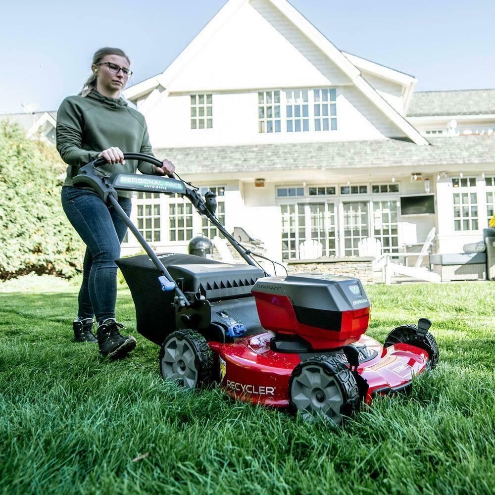 A woman is cutting the grass with a Toro push mower in front of a house.