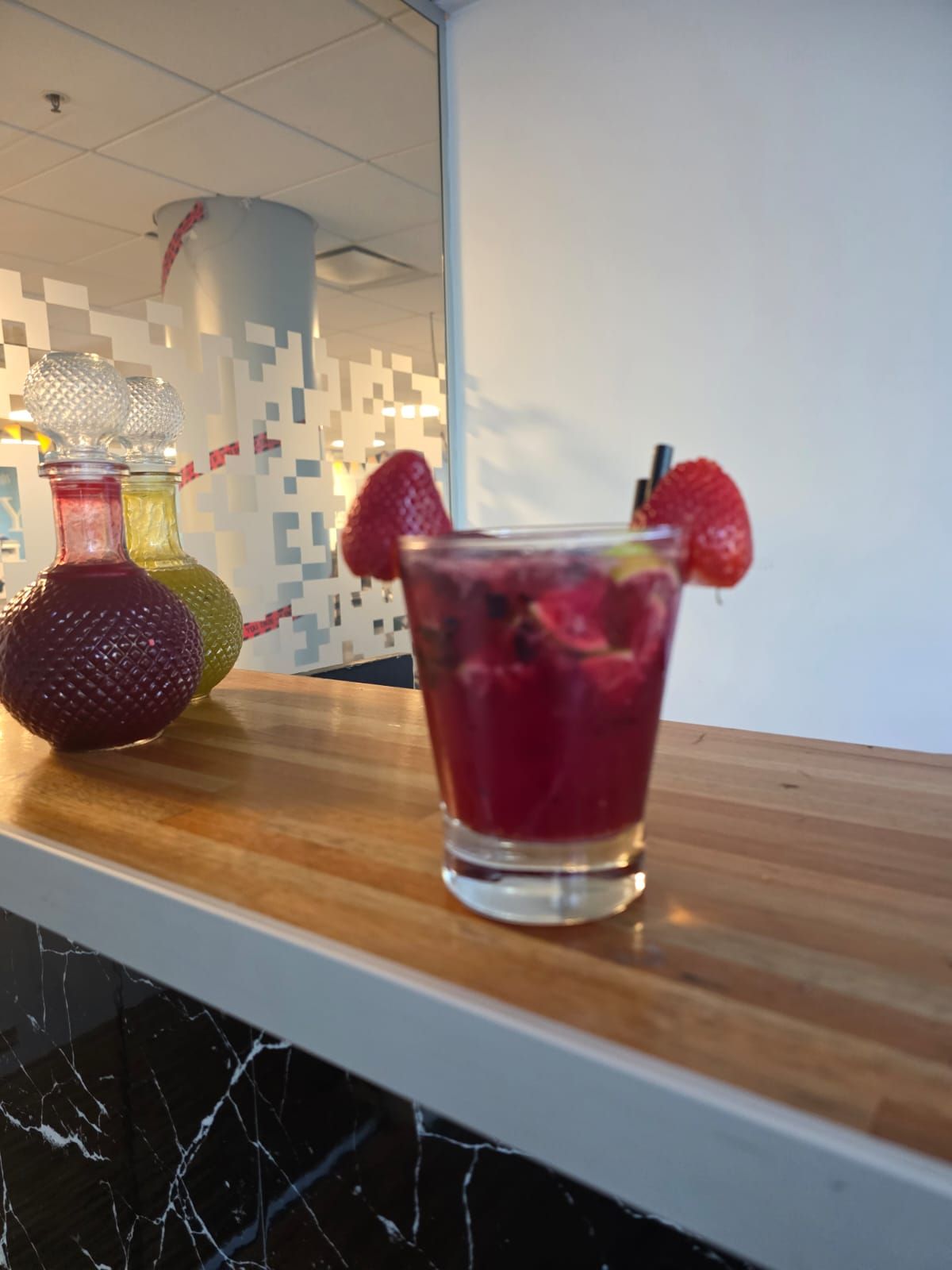 Cóctel de frutos rojos en un vaso con guarnición de fresa sobre una barra de madera, con una botella.