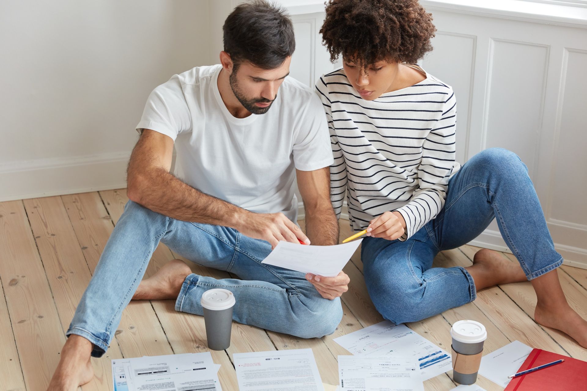 A man and a woman are sitting on the floor looking at a piece of paper.