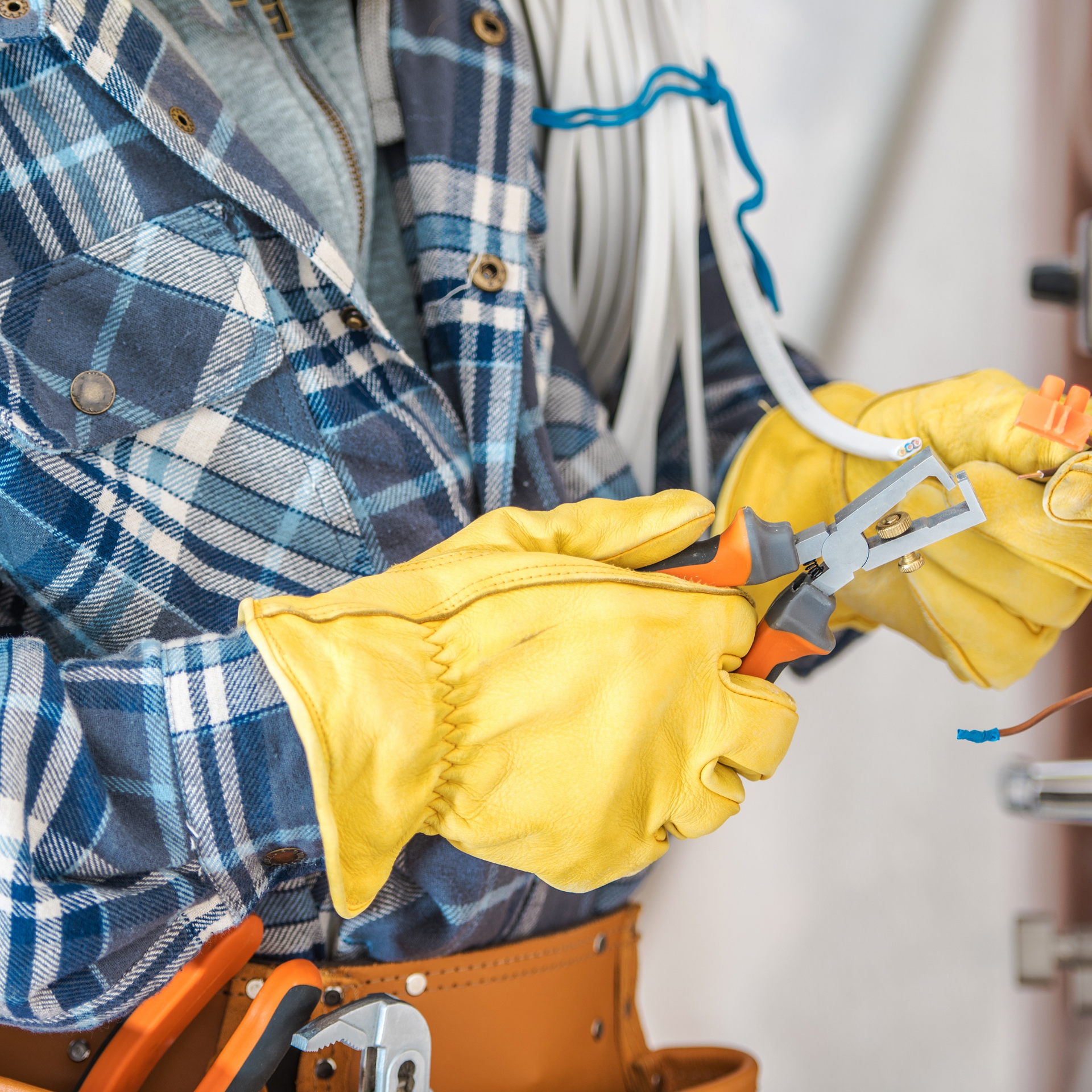 Electrician wearing gloves cutting wires with pliers.