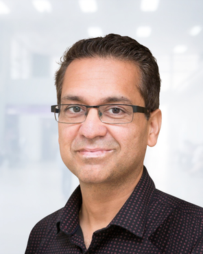 Portrait of a man wearing glasses and a dark shirt against a bright blurred background