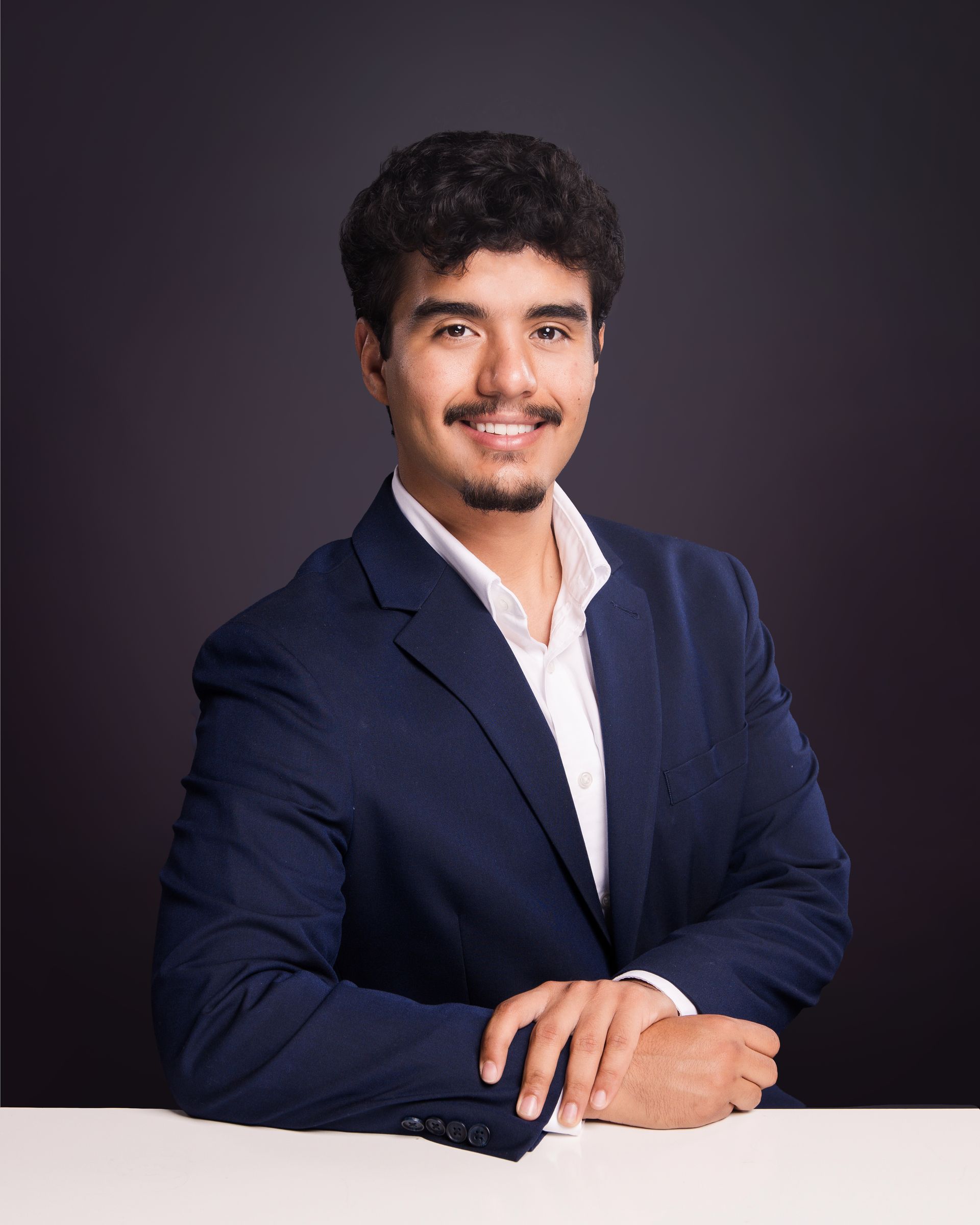 Portrait of a smiling person in a black blazer with arms crossed against a dark background