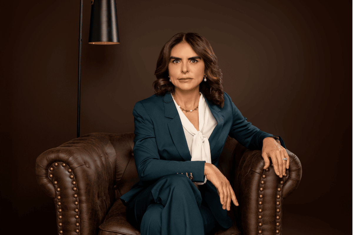 Portrait of a person in a teal suit seated in a brown leather armchair against a dark studio background