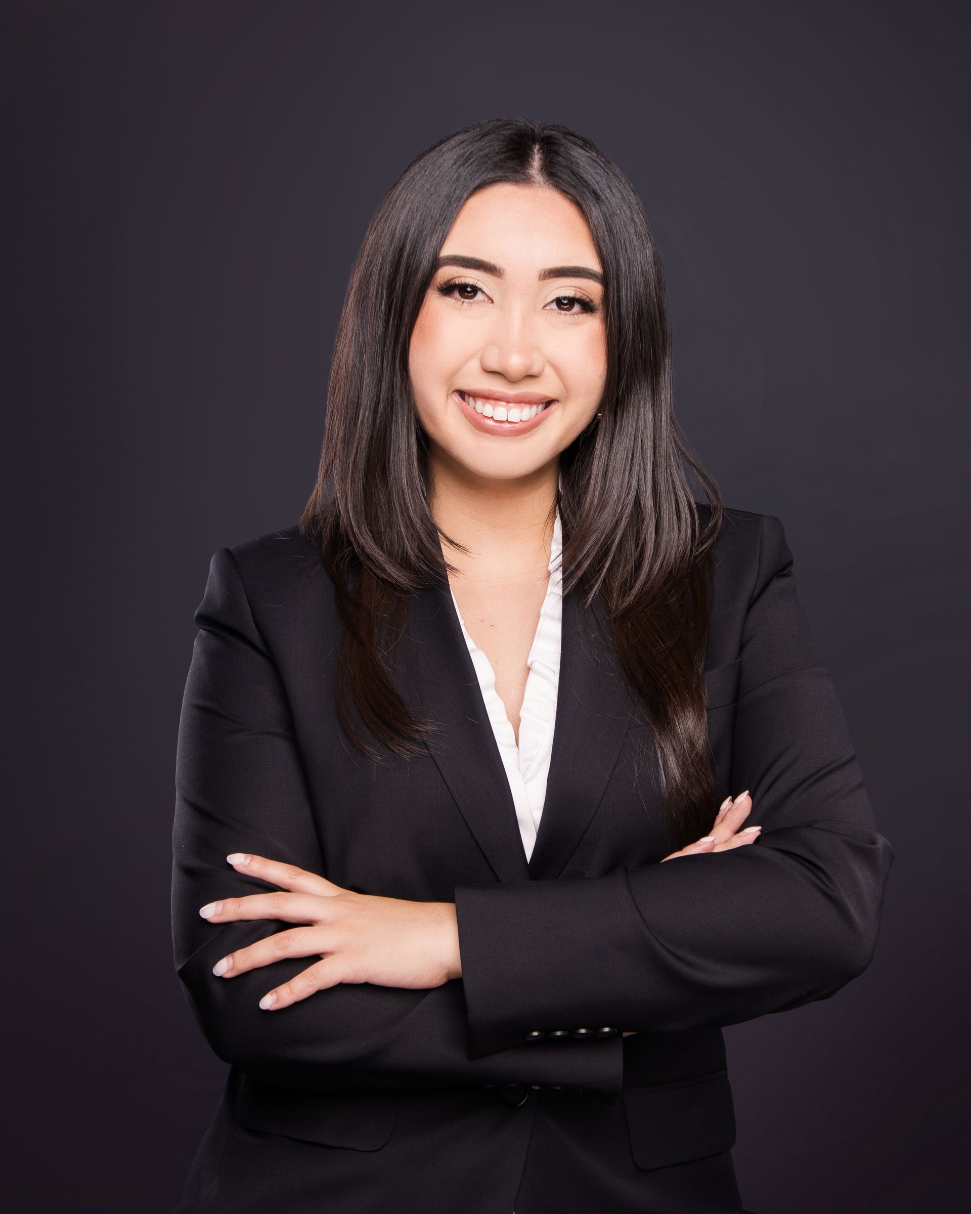 Portrait of a smiling person in a black blazer with arms crossed against a dark background
