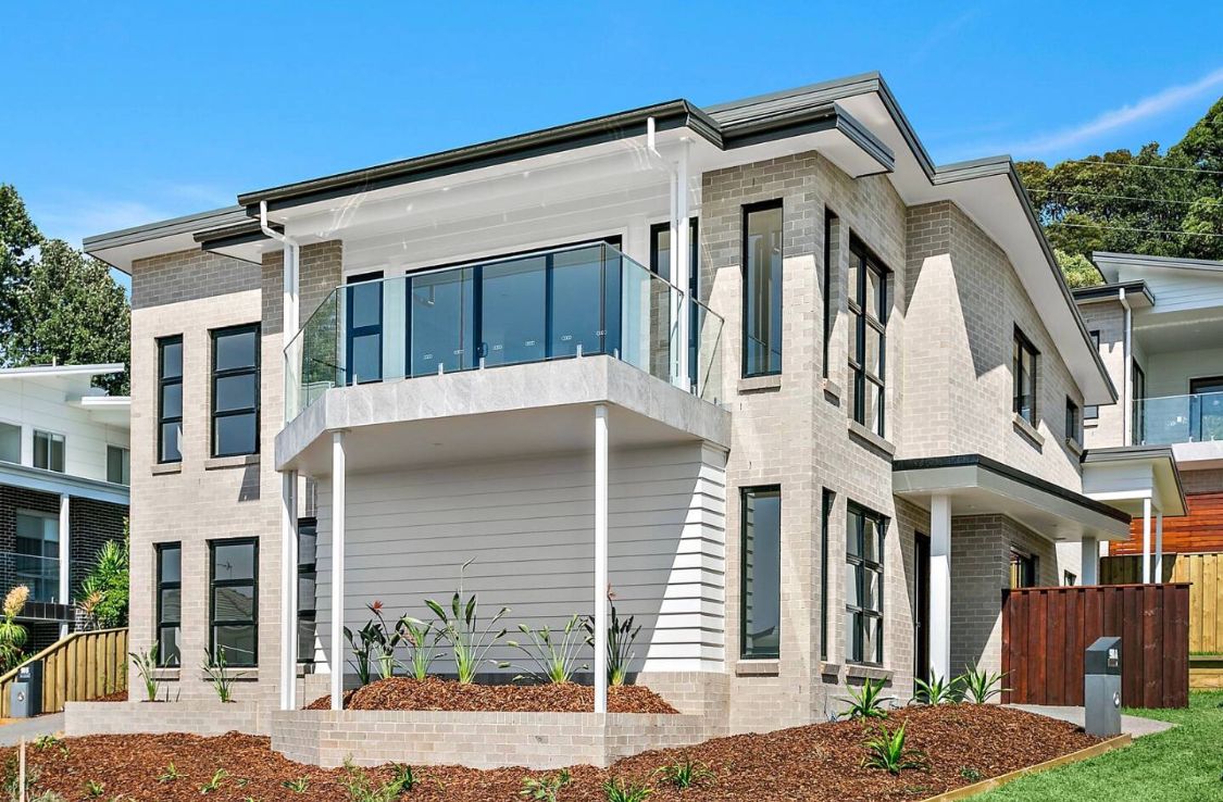 Two-story modern home with light brick exterior, balcony with glass railing, and blue sky — LG Constructions in Thirroul, NSW
