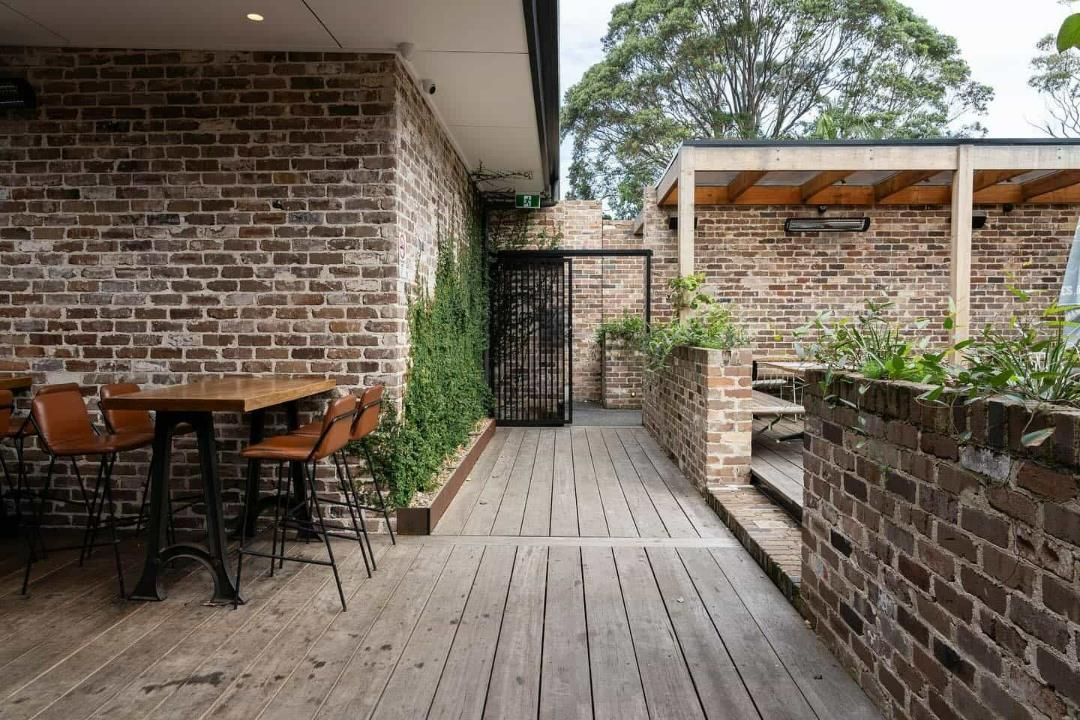 A Brick Building With a Wooden Deck and Tables and Chairs in Front of It — LG Constructions in Thirroul, NSW