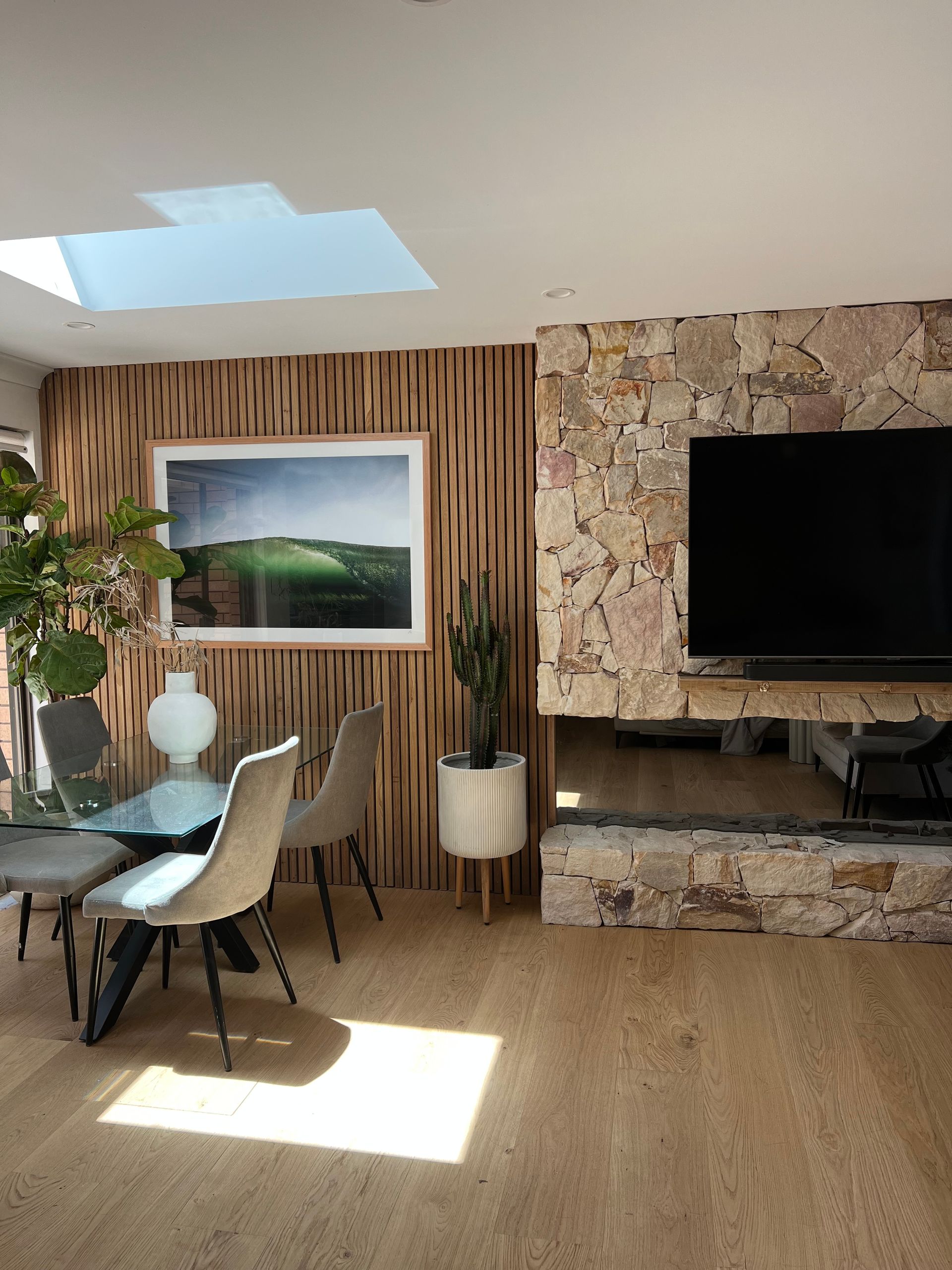 Dining room with wooden accent wall, stone fireplace, and natural light from skylight   — LG Constructions in Thirroul, NSW