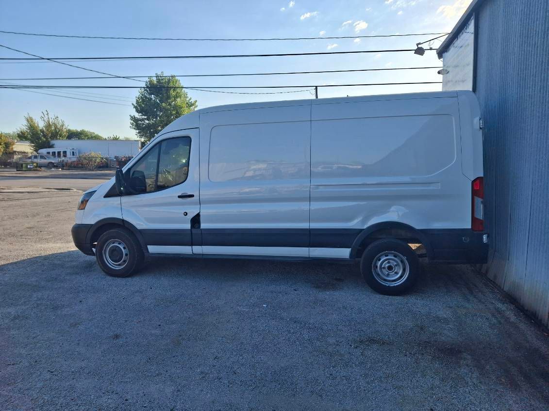 A white van is parked next to a building in a gravel lot.