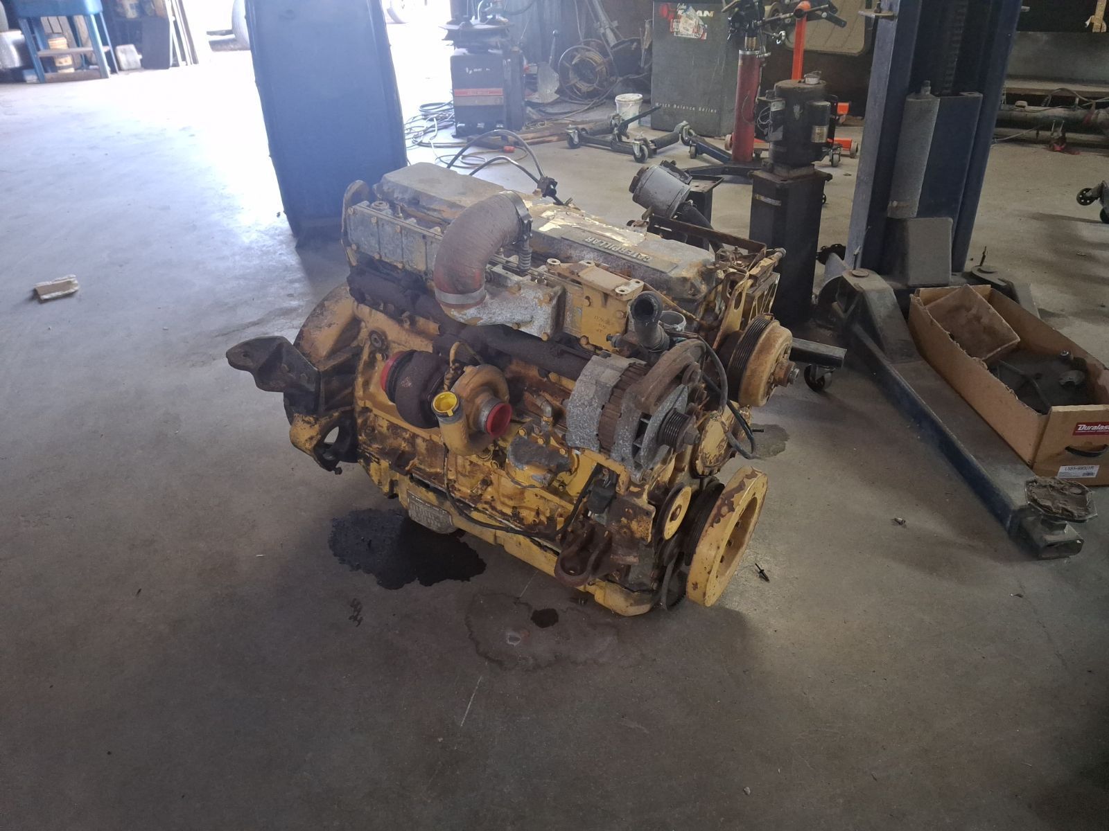 A yellow engine is sitting on the floor in a garage.